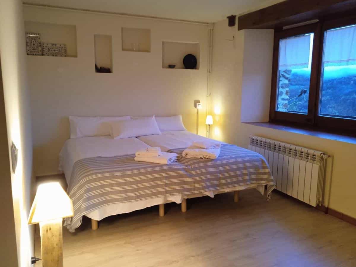 Bedroom with twin beds, striped blanket, and window view of dark, misty mountains. Casa Tapiolas Rectoría.