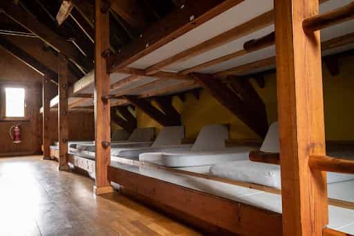 Wooden bunk beds with white mattresses inside an attic room with wood paneling and a small window.
