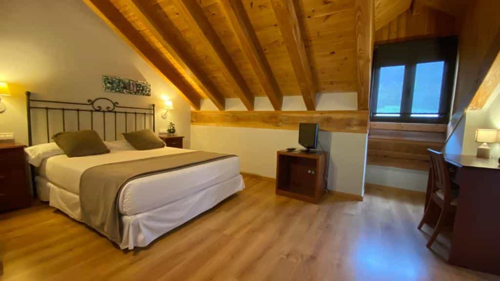 Attic hotel room with wood beams, large bed, and wooden floor in Roca Blanca area.