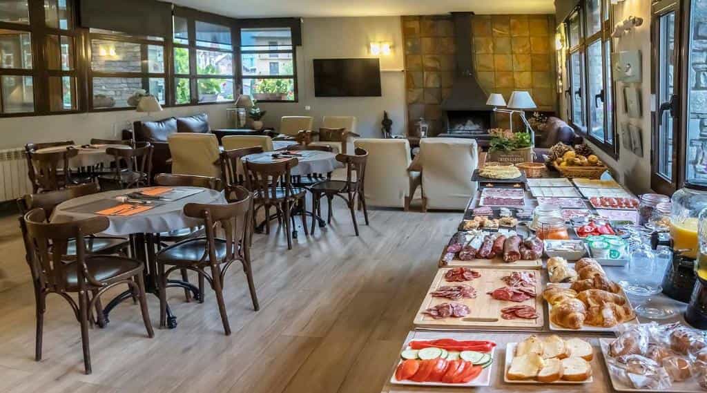 Breakfast buffet with meats, pastries, and fruit next to dining tables in a hotel lounge.