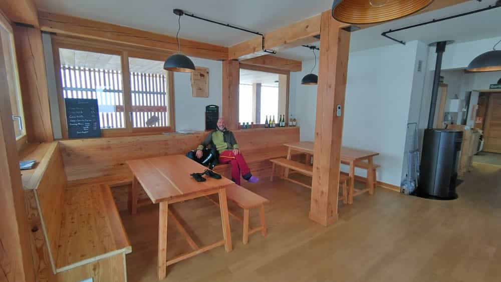 Man resting in wooden interior of Chalet-du-Clot with tables and wood stove