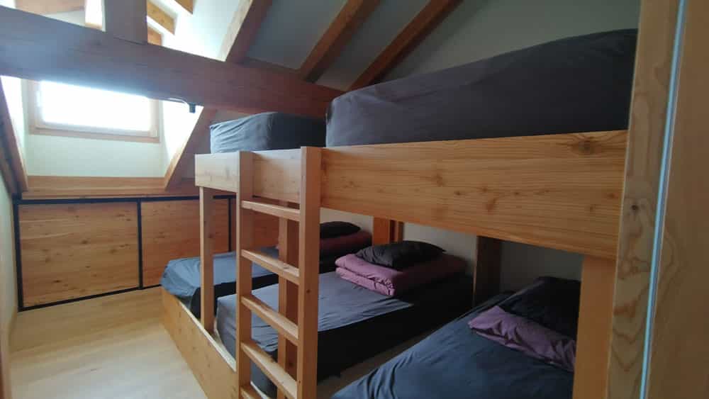 Wooden triple bunk beds in an attic room with sloped ceiling and exposed beams at Chalet du Clot.