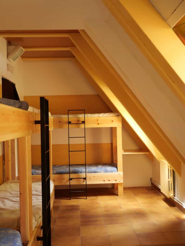 Wooden bunk beds in an attic room with sloped ceiling beams and tiled floor.