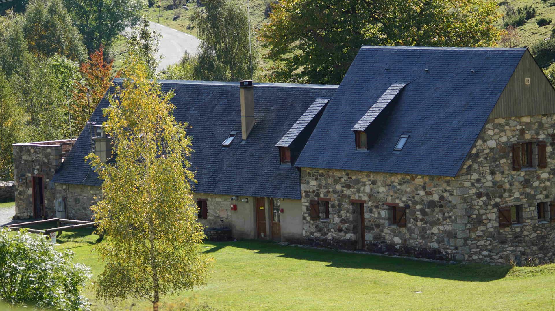 Stone refuge with dark slate roof in grassy mountain setting, Refugio de la Grange de Holle.
