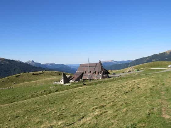 Refuge building on grassy mountain slope with distant peaks under clear blue sky, Belagua.