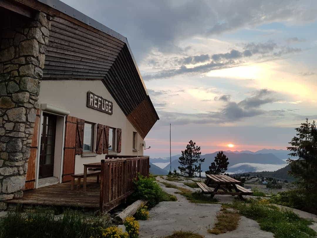 Refuge building with wooden deck overlooking mountains at sunset, Jeandel location.