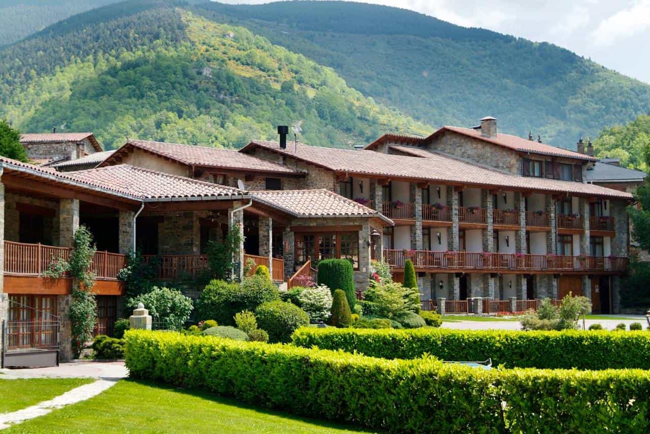Stone hotel with wooden balconies set against lush green mountainside, Hotel La Coma.
