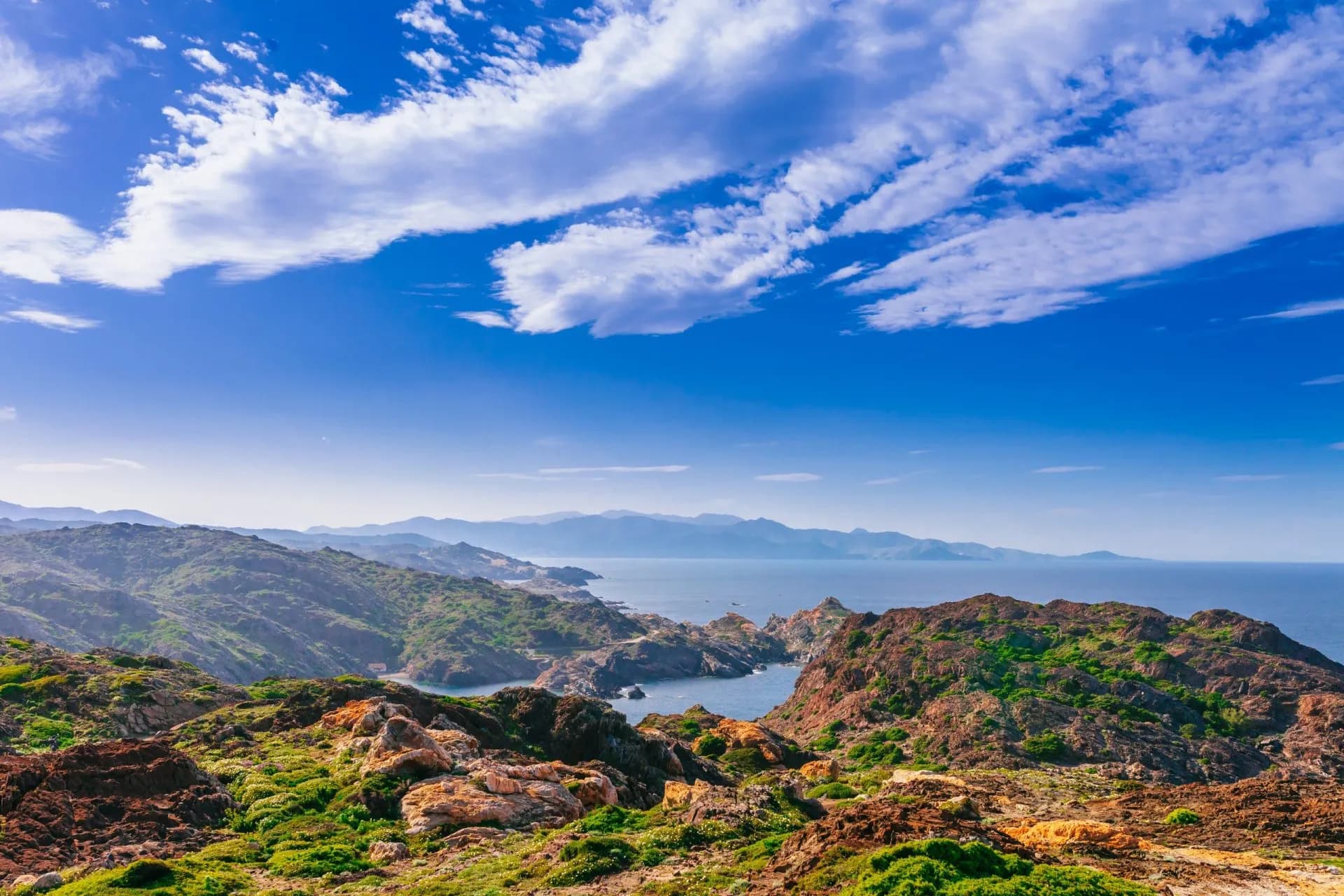 Rocky Cap de Creus coastline overlooking the Mediterranean Sea under a blue sky with white clouds.
