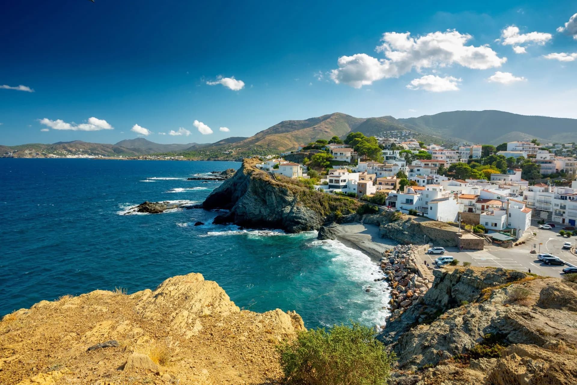 Coastal town with white buildings on rocky cliffs overlooking deep blue Mediterranean Sea near Llanca.