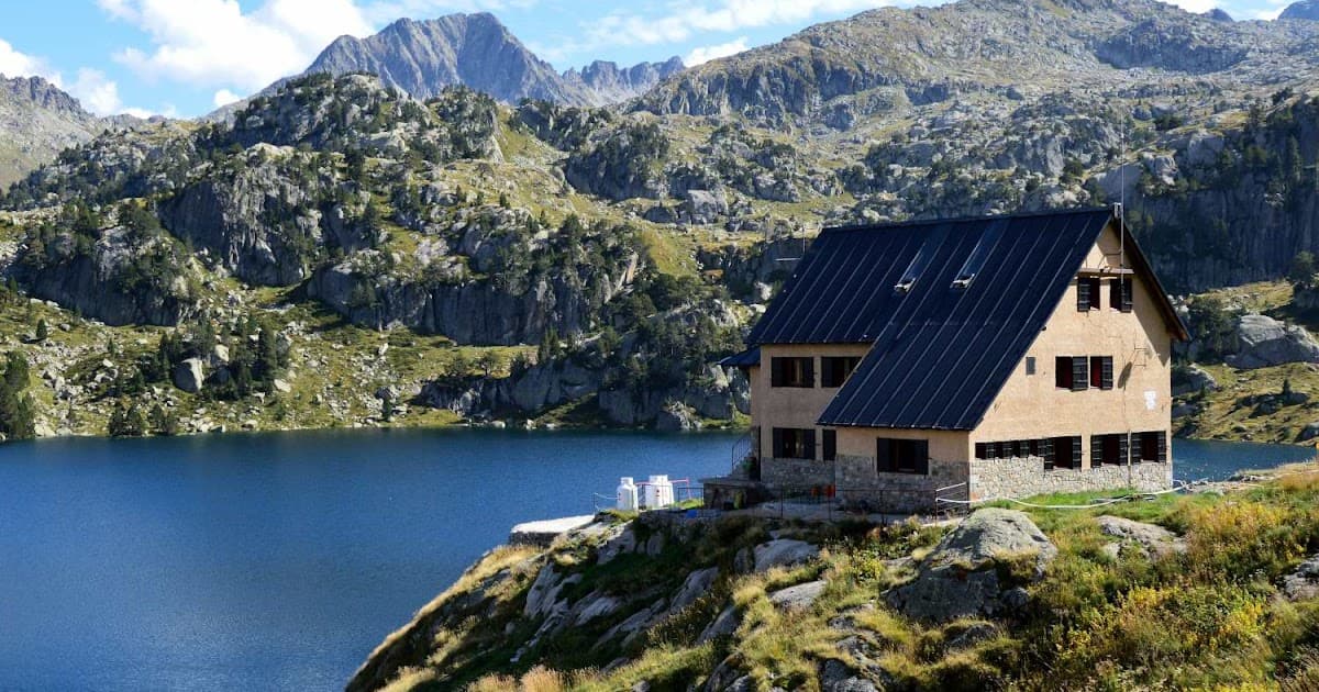 Mountain refuge hut beside deep blue alpine lake with rocky peaks in background