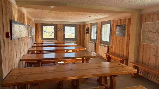 Refugio de Góriz dining hall with wooden tables and mountain views through windows.