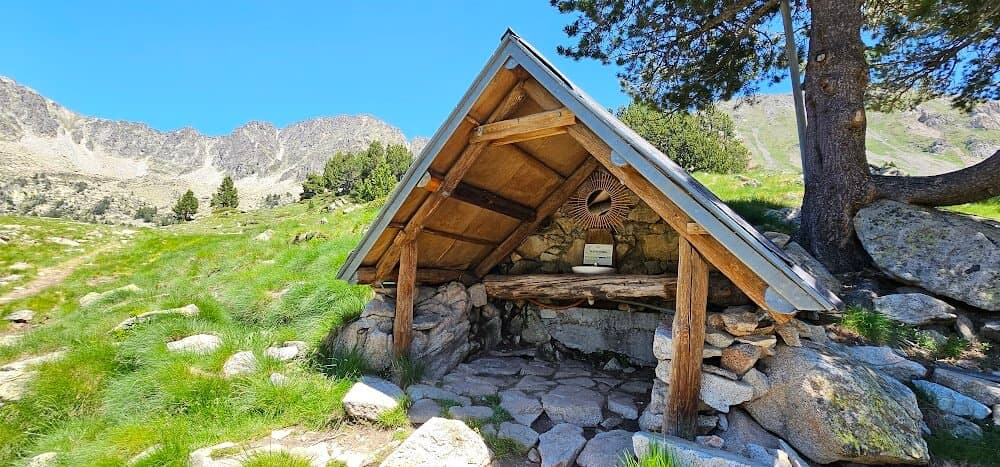 Rustic wooden shelter with stone base on grassy mountain trail near Refuge de Bastan.