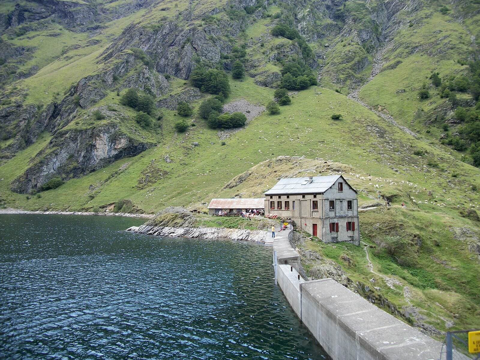 Refuge Lac d'Oô next to dark water with steep grassy mountain slopes.