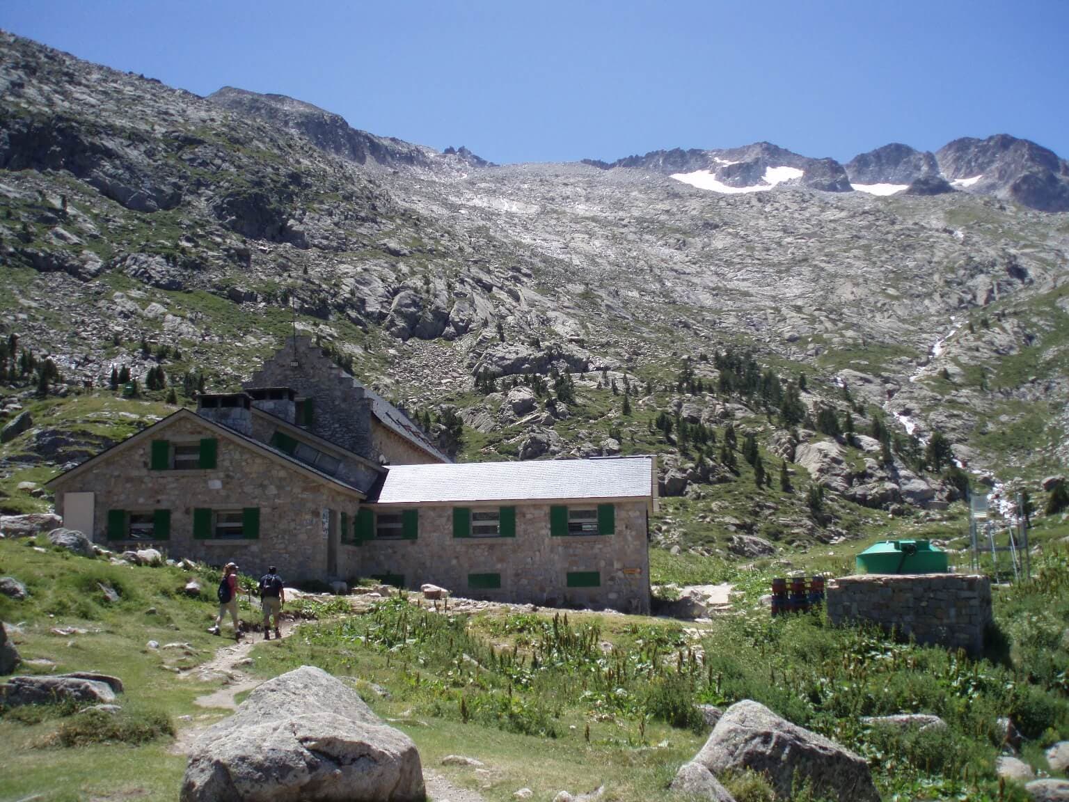 Refugio de la Renclusa stone mountain refuge with hikers below rocky peaks and snow patches