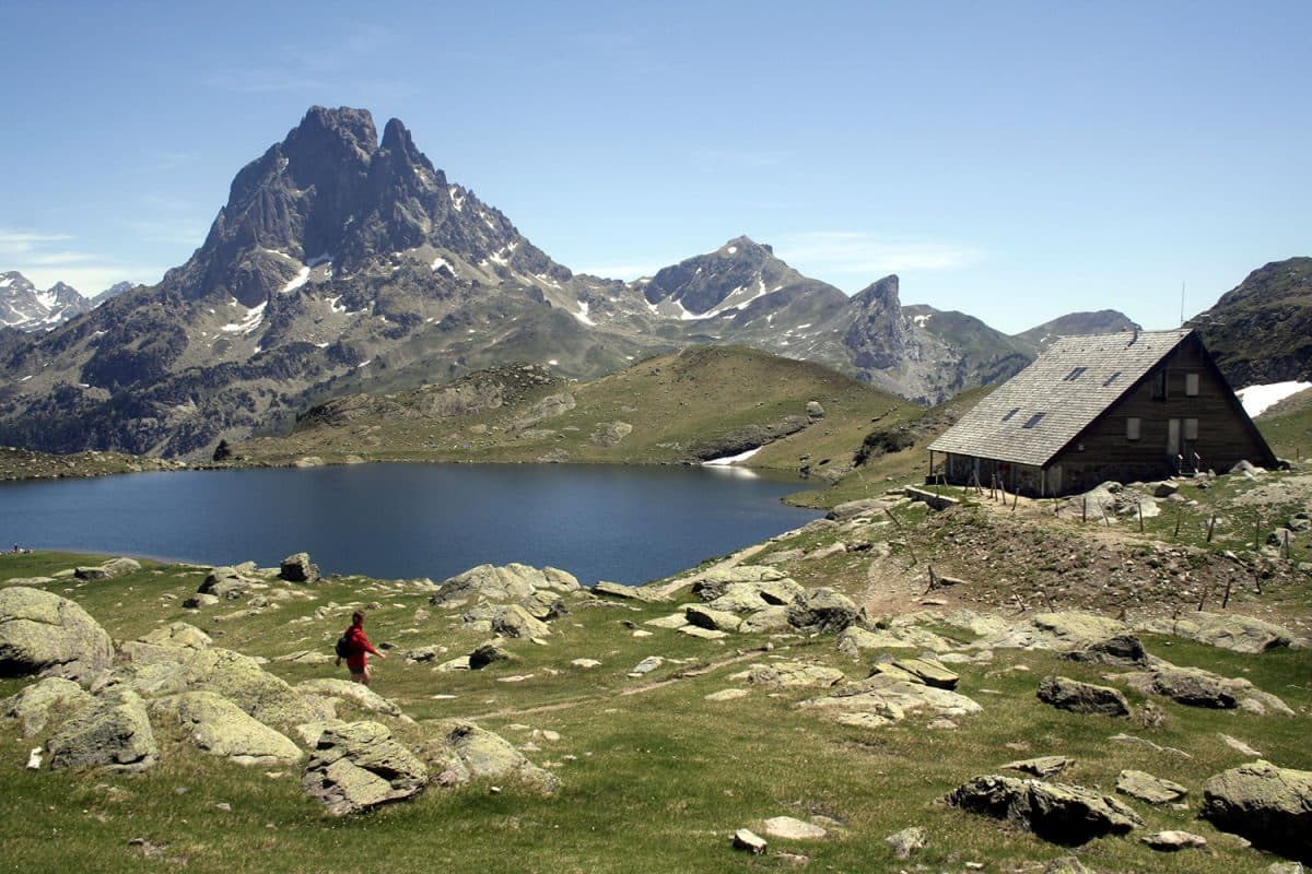 Hiker near Refuge Ayous by Pic du Midi d'Ossau and mountain lake.