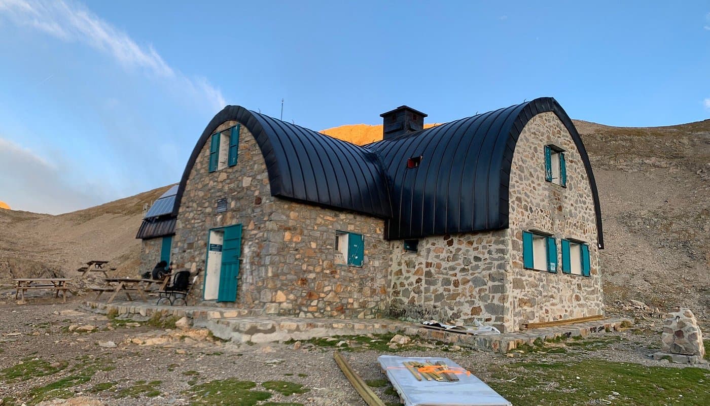 Stone mountain refuge with curved black roof and teal shutters in barren landscape