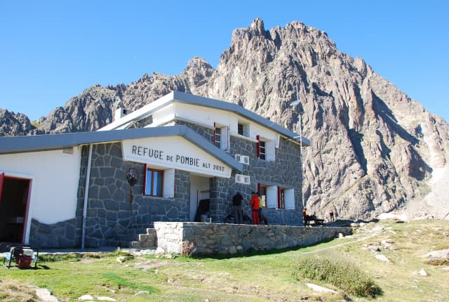 Refuge de Pombie mountain hut at 2052m altitude against rugged peaks under clear sky.