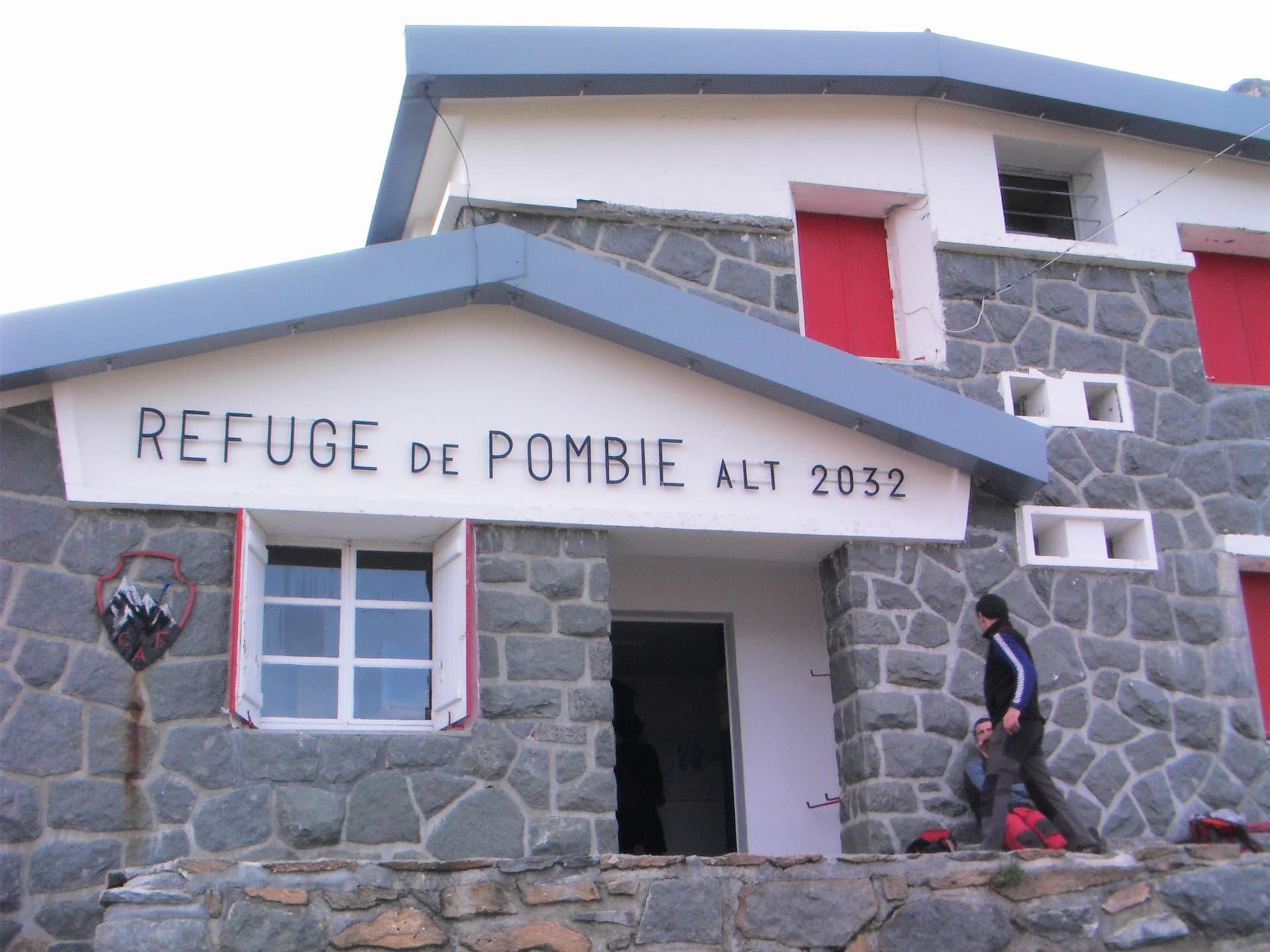 Refuge de Pombie entrance, stone building with red shutters, hikers arriving at altitude 2032.