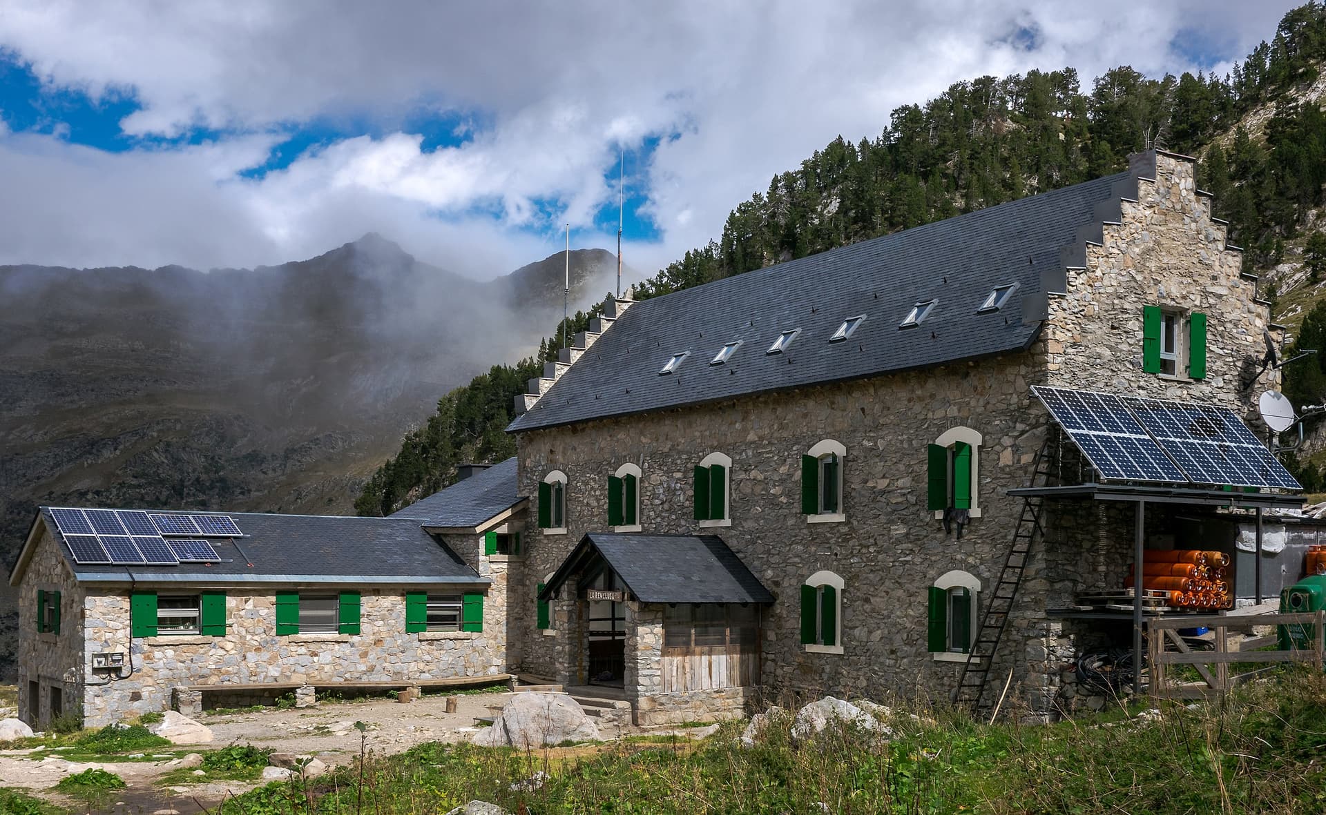 Refugio de la Renclusa stone mountain hut with solar panels against foggy peaks.