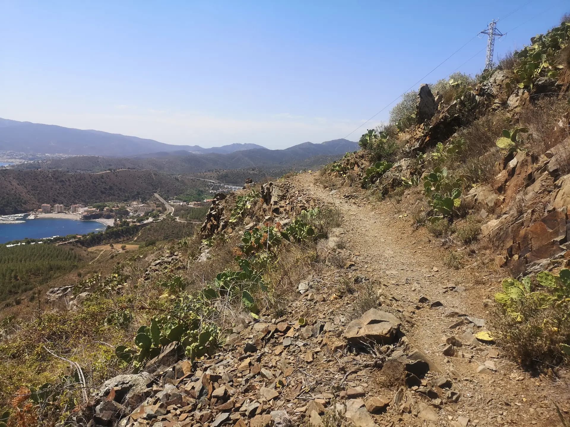 Hiking trail on a rocky hillside overlooking a coastal bay and mountains.