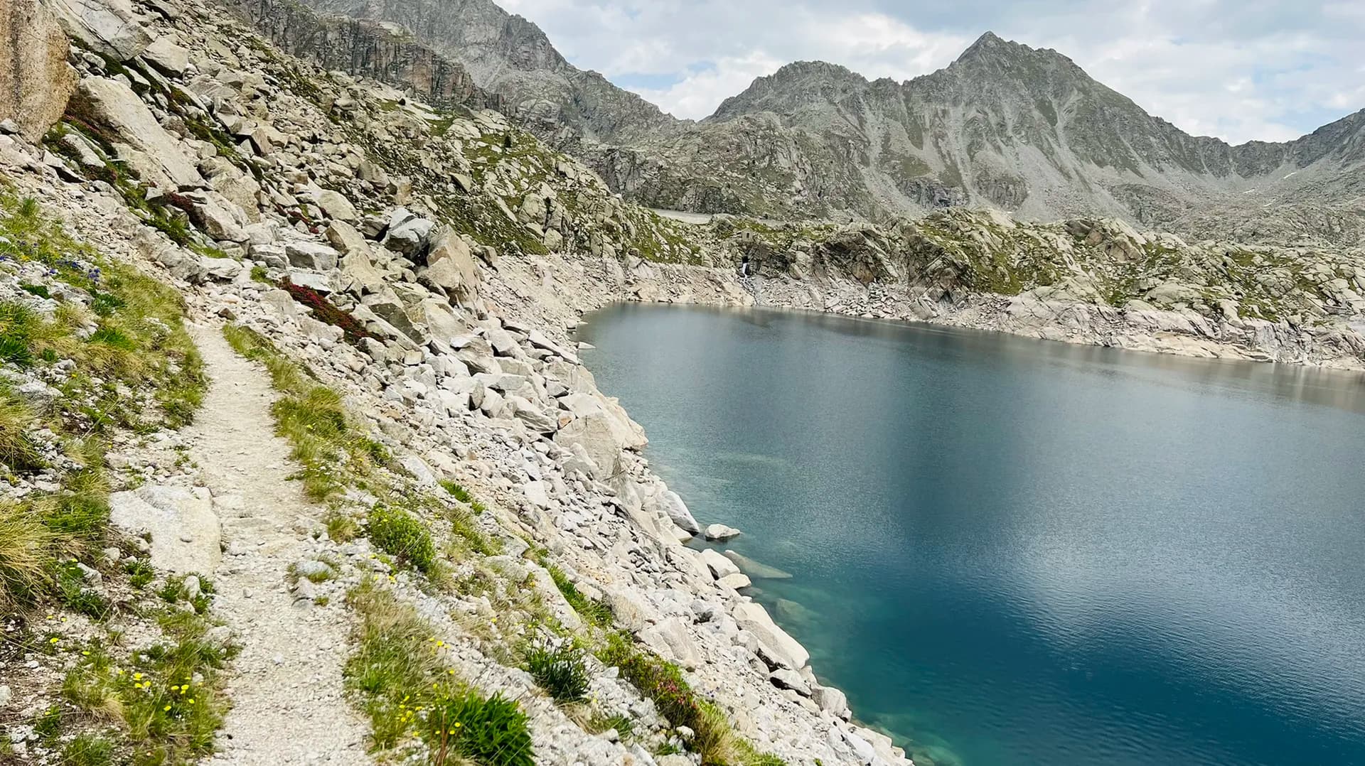 Hiking trail along a rocky alpine lake surrounded by mountain peaks.