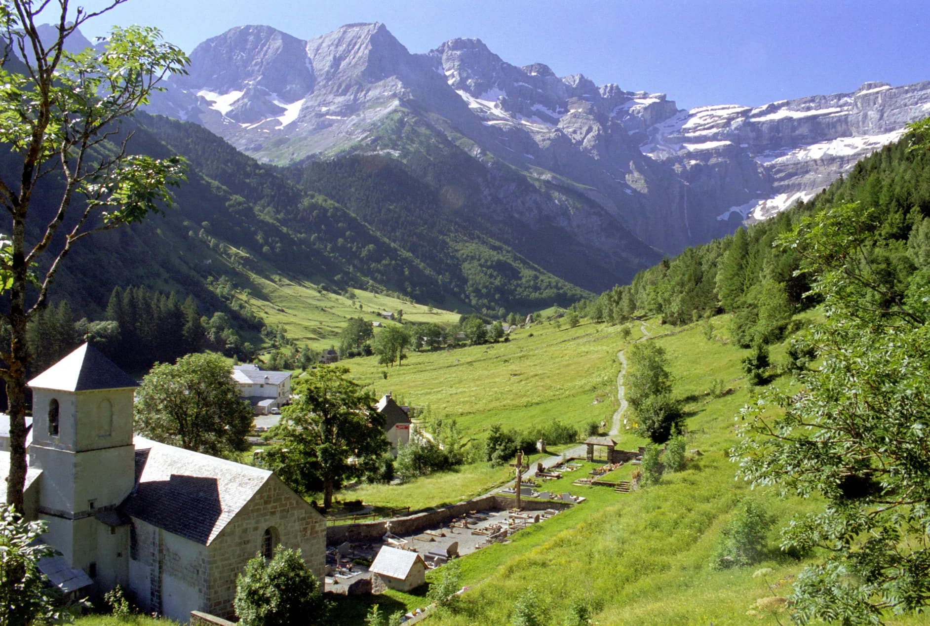 Stone church and cemetery in the green Valley of Gavarnie beneath snow-capped Pyrenees mountains.