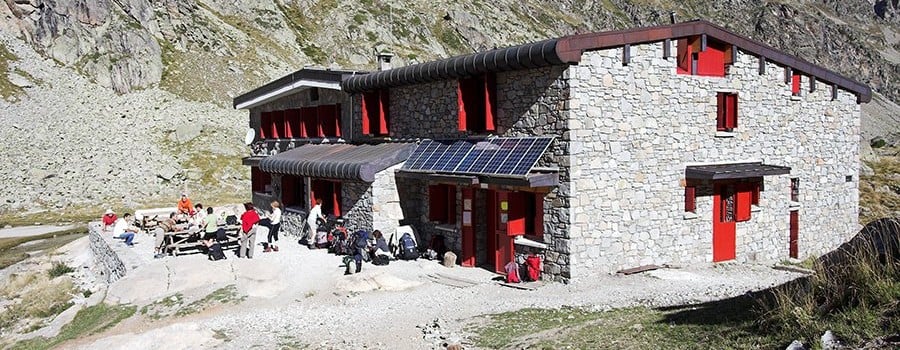 Refuge des Oulettes de Gaube stone mountain hut with hikers resting outside against rocky terrain.