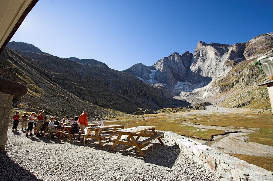 Hikers resting at picnic tables with massive rocky mountains and glacier visible in the distance.