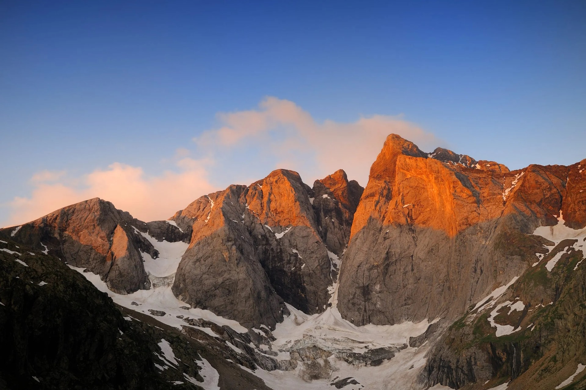 Vignemale glacier and rocky peaks illuminated by sunrise under a blue sky.