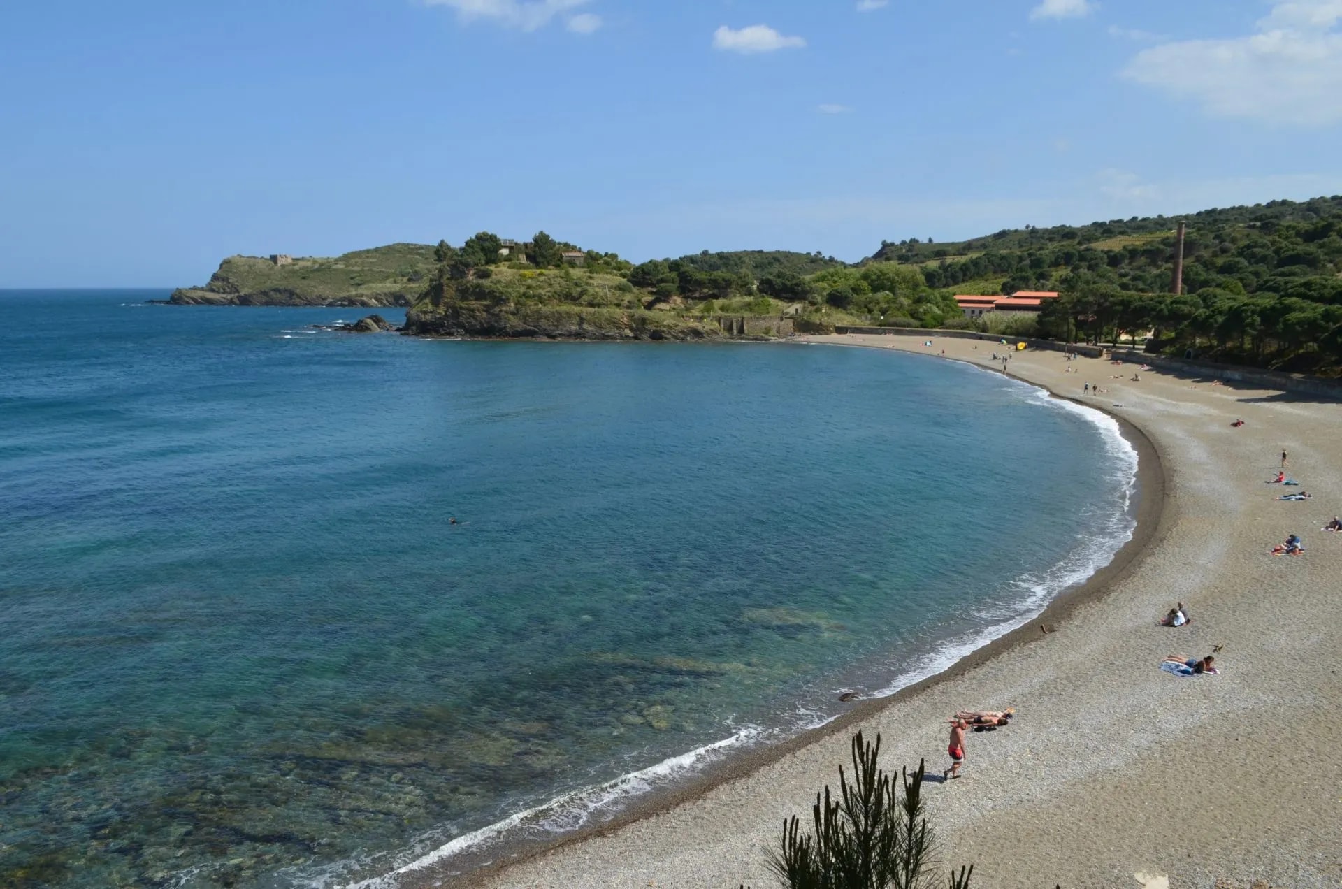 Plage de Paulilles pebble beach with clear blue water and sunbathers on a sunny day.