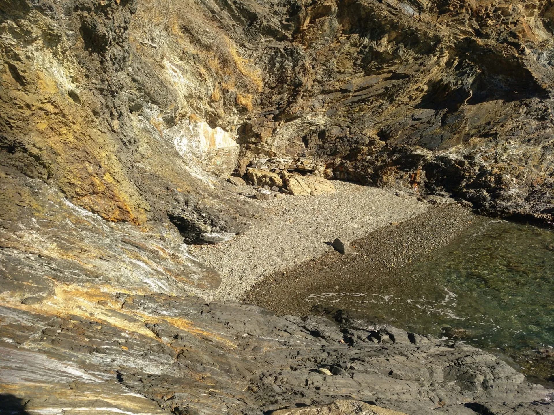 Secluded pebble beach nestled between steep, colorful cliffs near Portbou, meeting clear sea water.