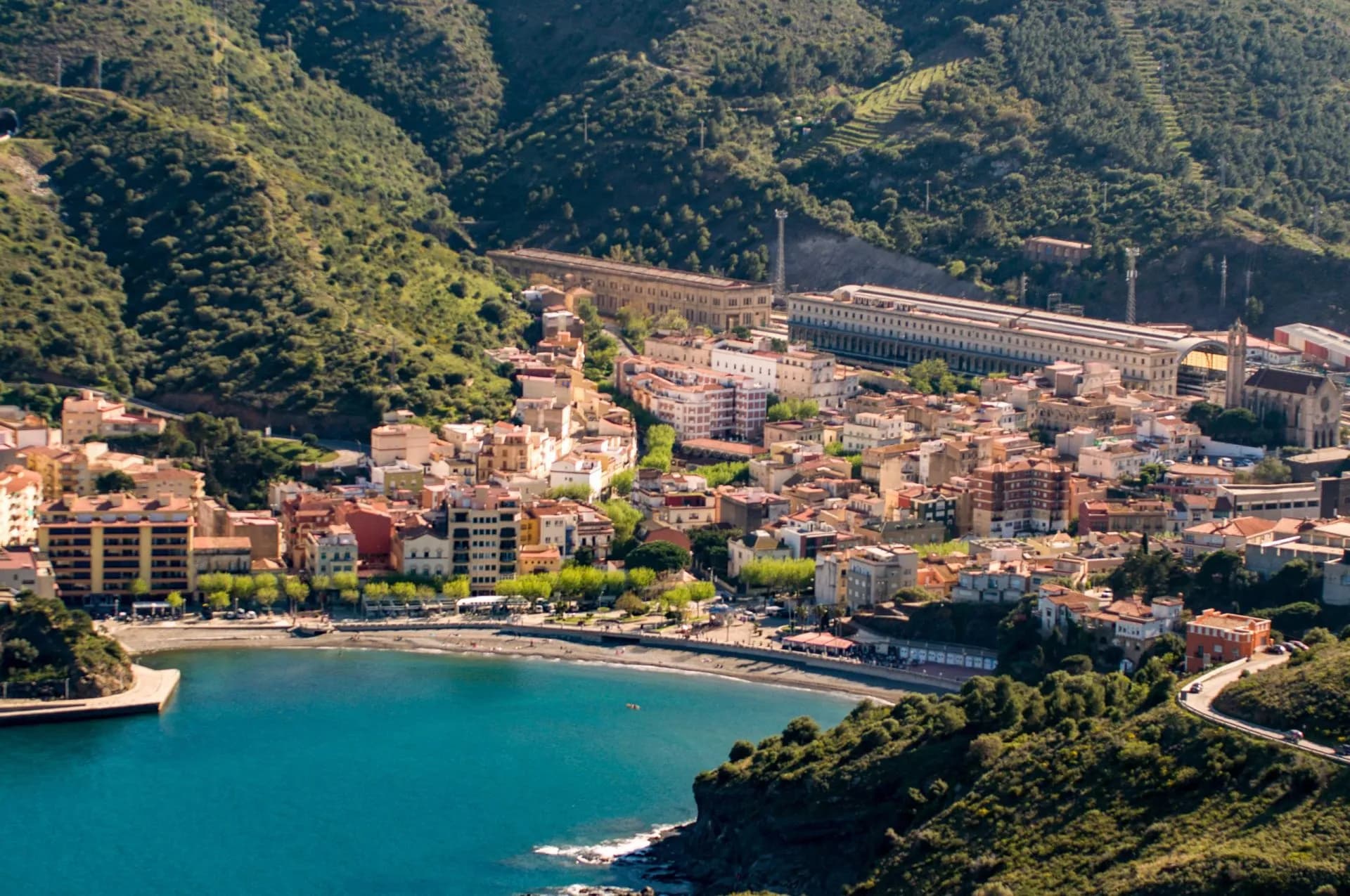 Coastal town of Portbou nestled between steep, green hills and a turquoise bay.