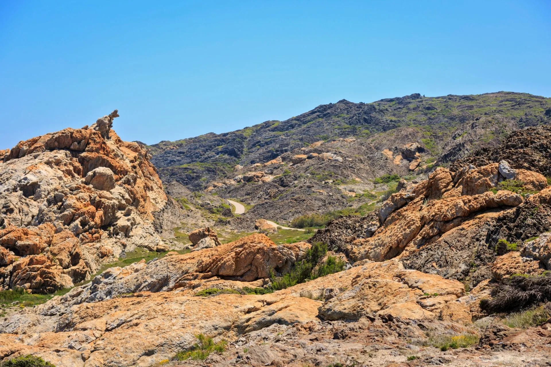 Cap de Creus National Park landscape with rugged orange rocks and winding road under clear blue sky.