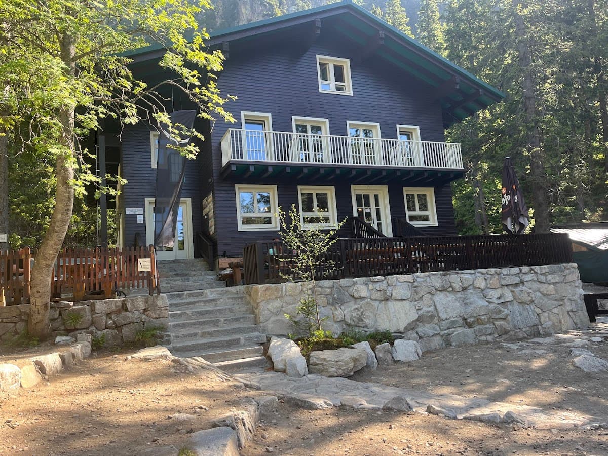 Dark wooden mountain lodge with white balcony railings surrounded by forest and stone steps.