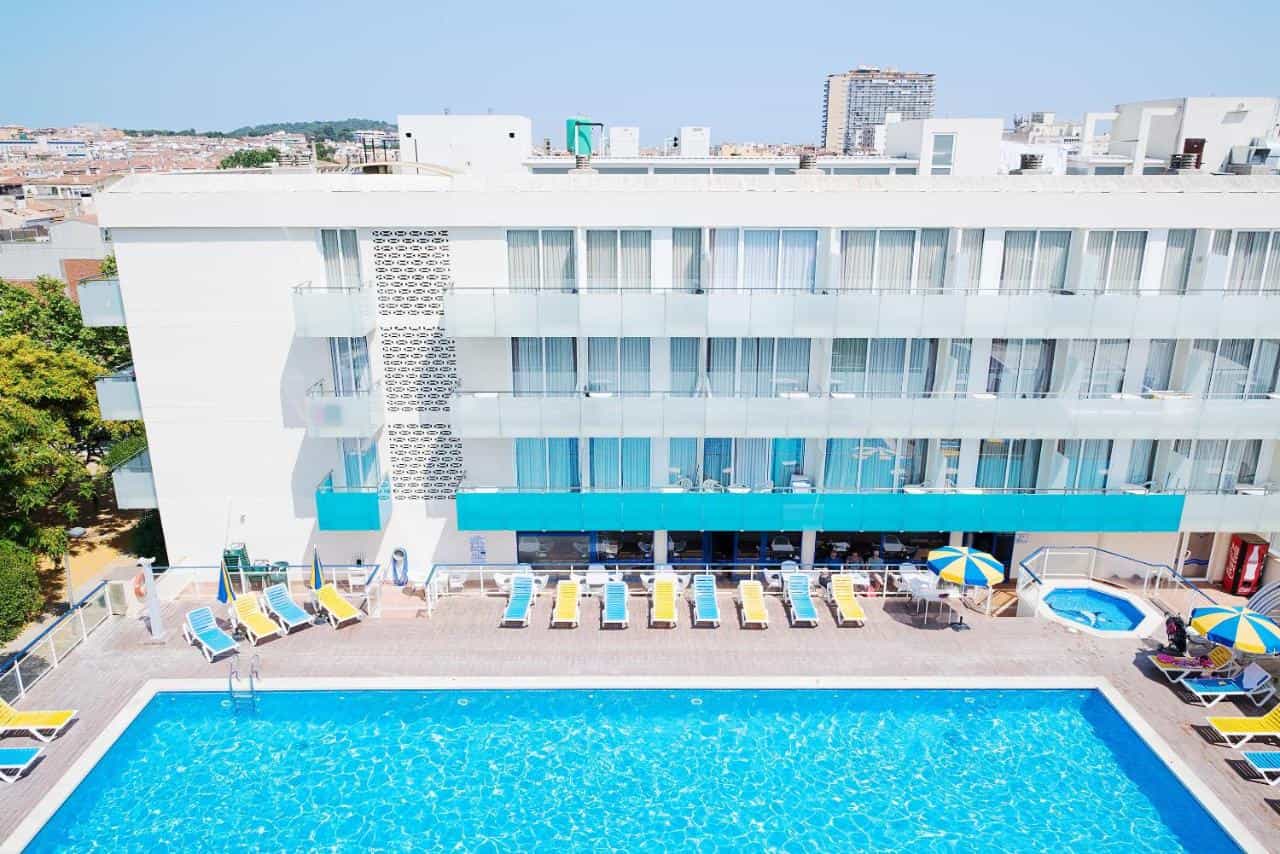 Aparthotel Ona Palamós exterior with large swimming pool, sun loungers, and city view.