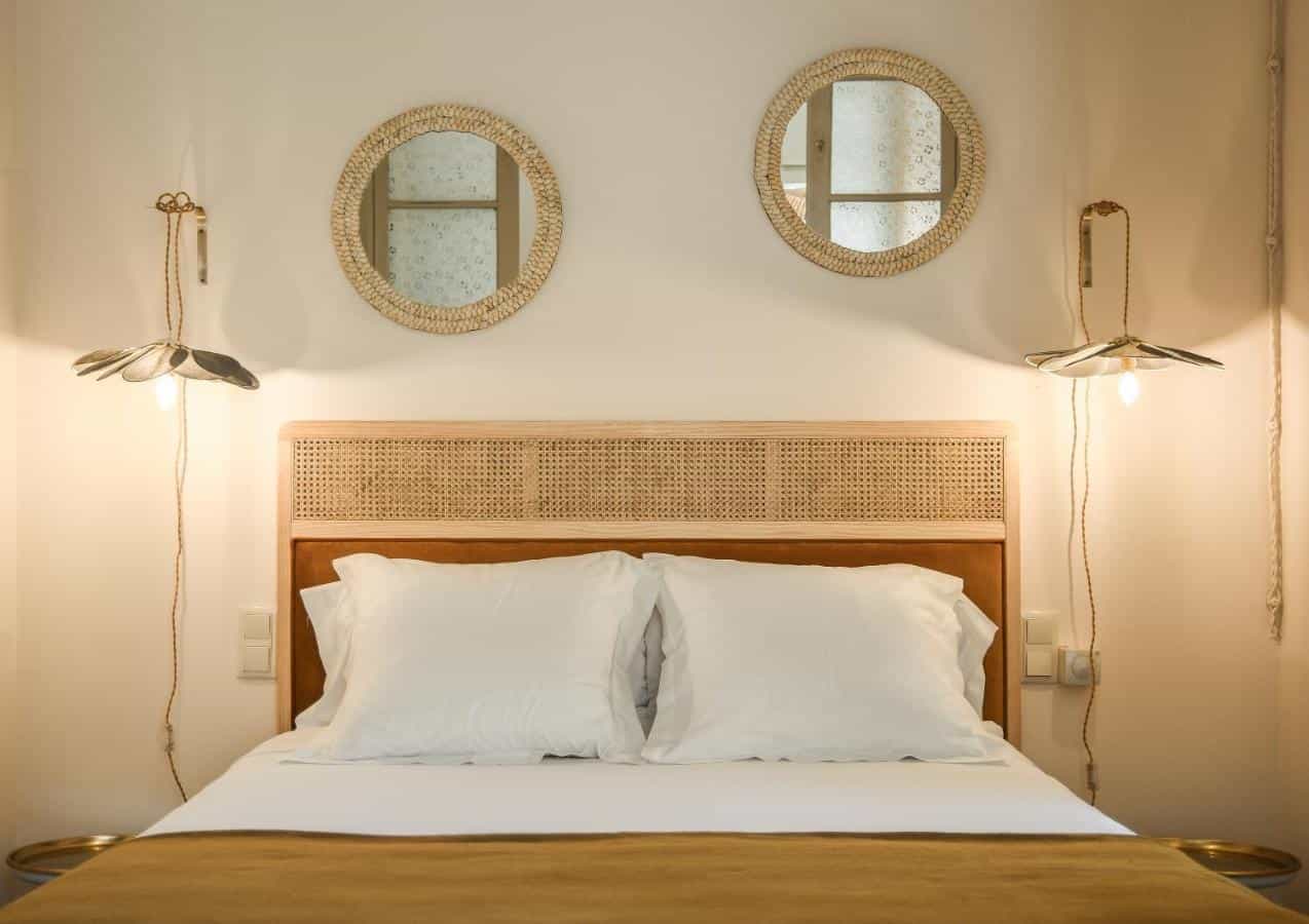 Hotel Aiguaclara room with white bedding, rattan headboard, and woven mirrors.