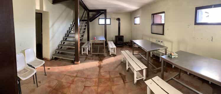 Interior of Refugio Viadós with metal tables, white benches, wood stove, and metal stairs.