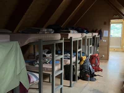Bunk beds with mattresses and gear in a wooden attic room at Refugio Ángel Orús mountain hut.