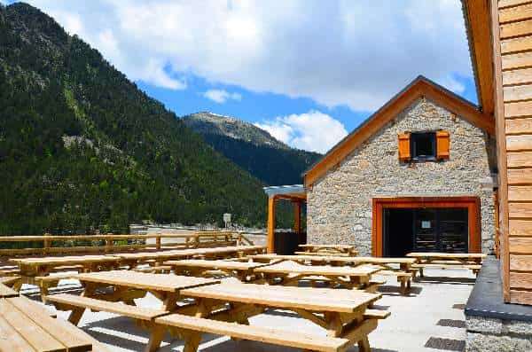 Picnic tables outside stone refuge with forested mountains at Refuge Lac de l’Oule
