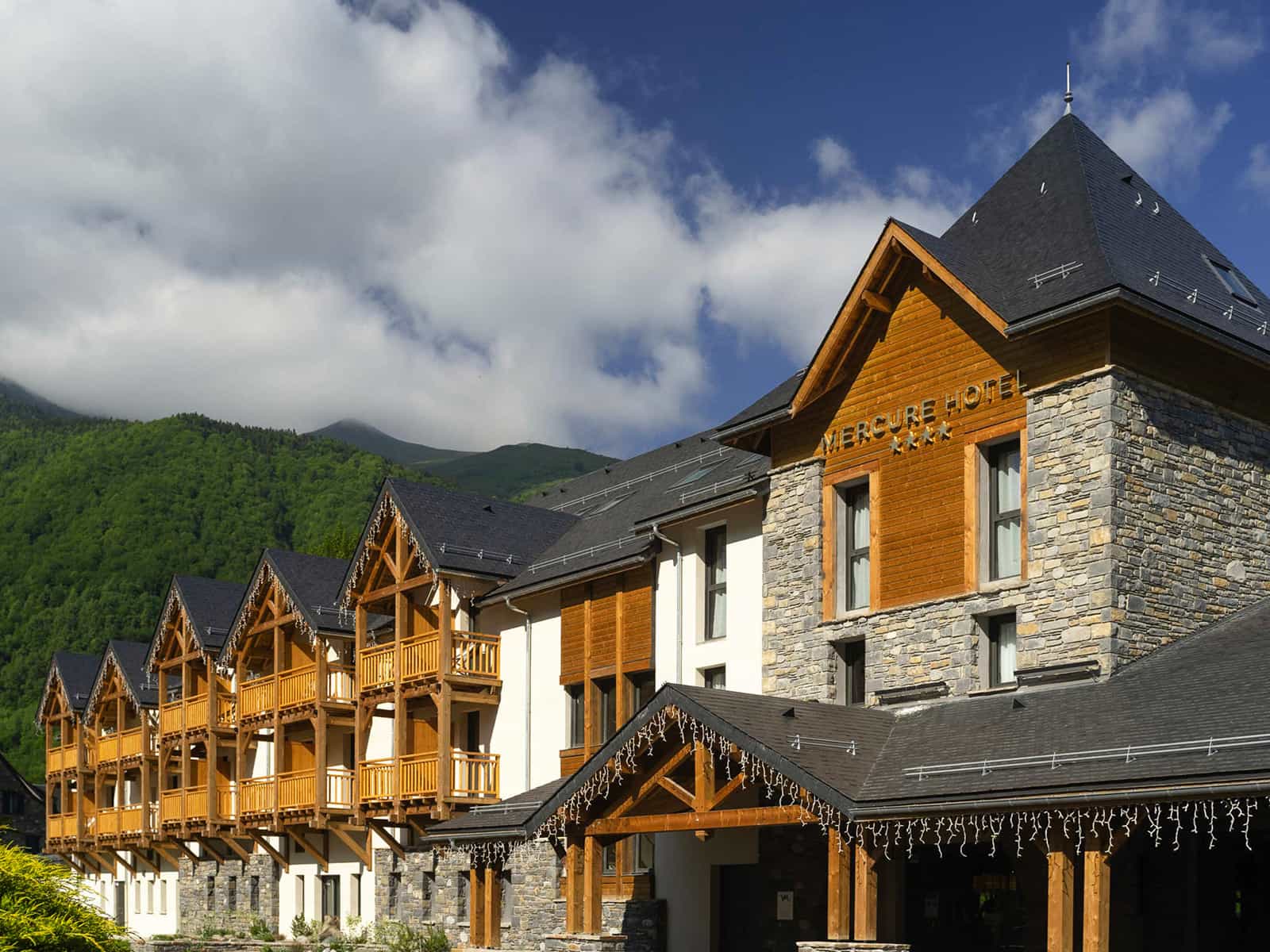Mercure Hotel Loudenvielle Pyrenees Peyragudes building with wooden balconies against green mountains.