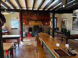 Rustic dining hall interior with long wooden tables, exposed beams, and stone fireplace at Le Refuge d'Espingo.