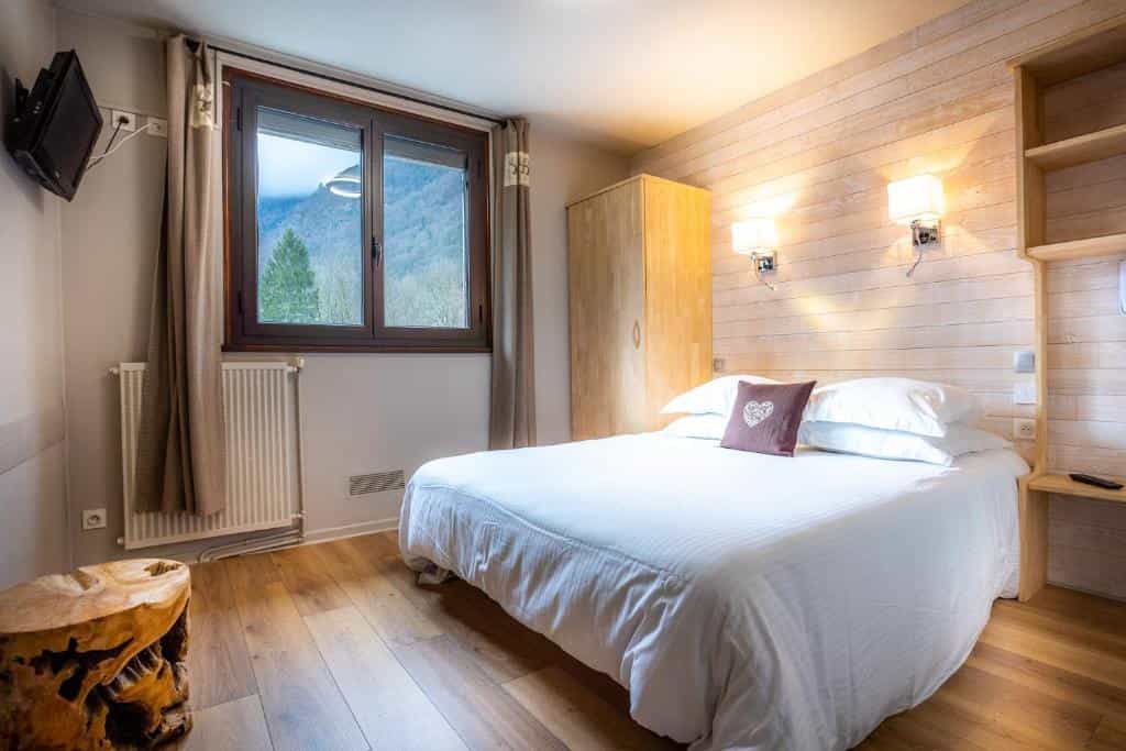 Bedroom with white bedding, wood paneling, and mountain view through window at Hôtel La Rencluse.