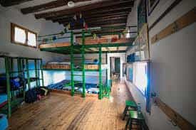 Bunk beds with green metal frames in a rustic mountain refuge room with wooden floors.