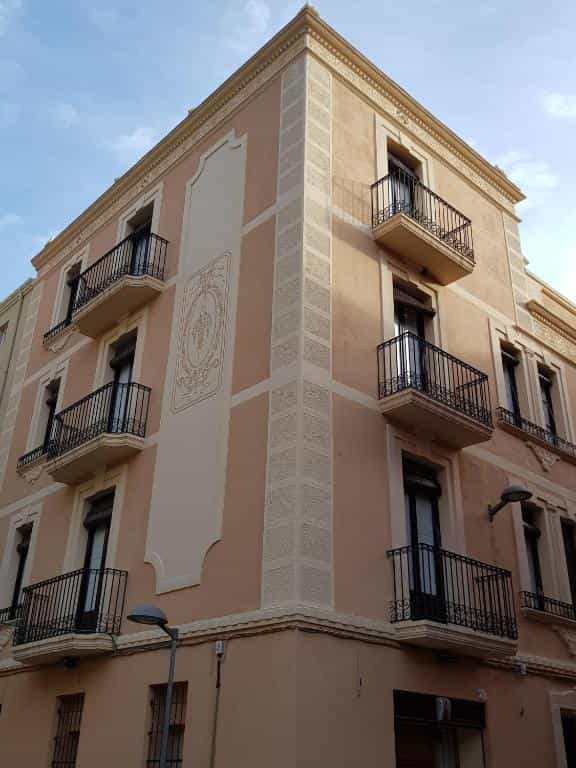 Apartaments Nouvilas building corner with pink facade, wrought iron balconies, and decorative stucco under blue sky.