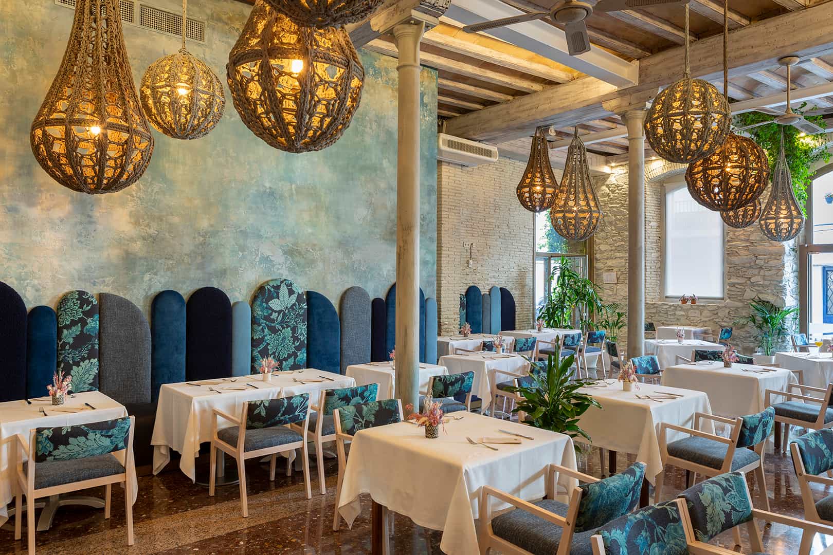 Restaurant dining area with woven pendant lights, blue seating, and white tablecloths in Porto Cristo.