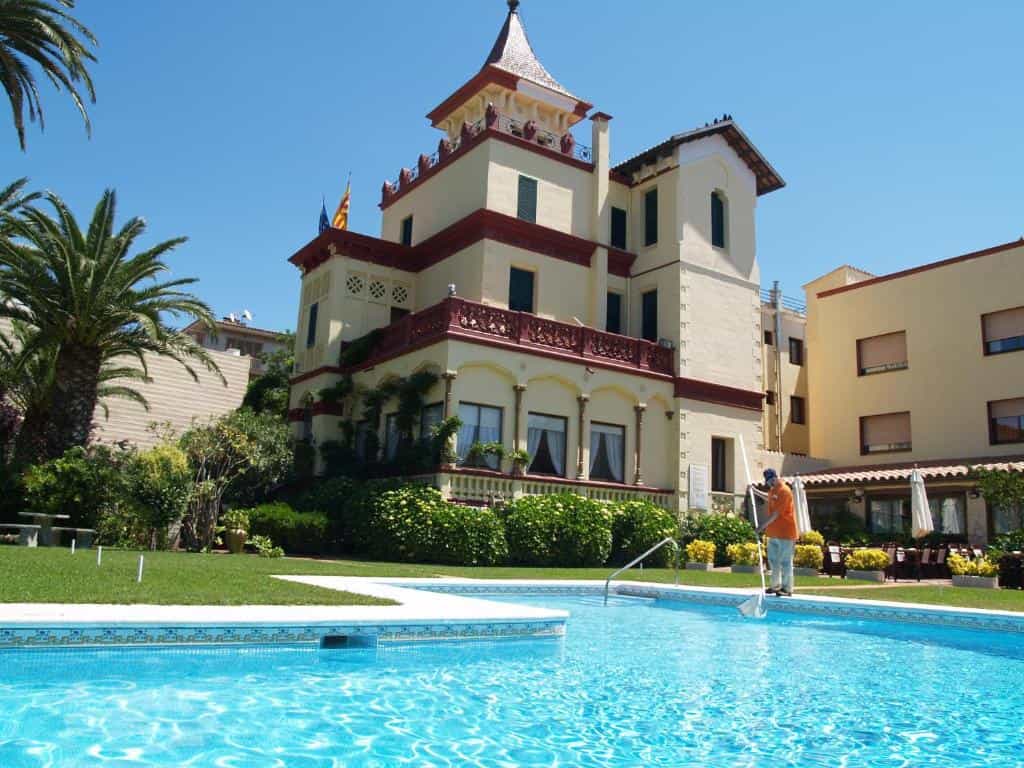 Pool maintenance worker cleaning pool by Hotel-Hostal del Sol under clear blue sky.