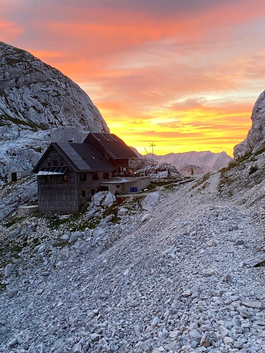 Mountain refuge hut among rocky terrain at sunrise with orange and yellow sky