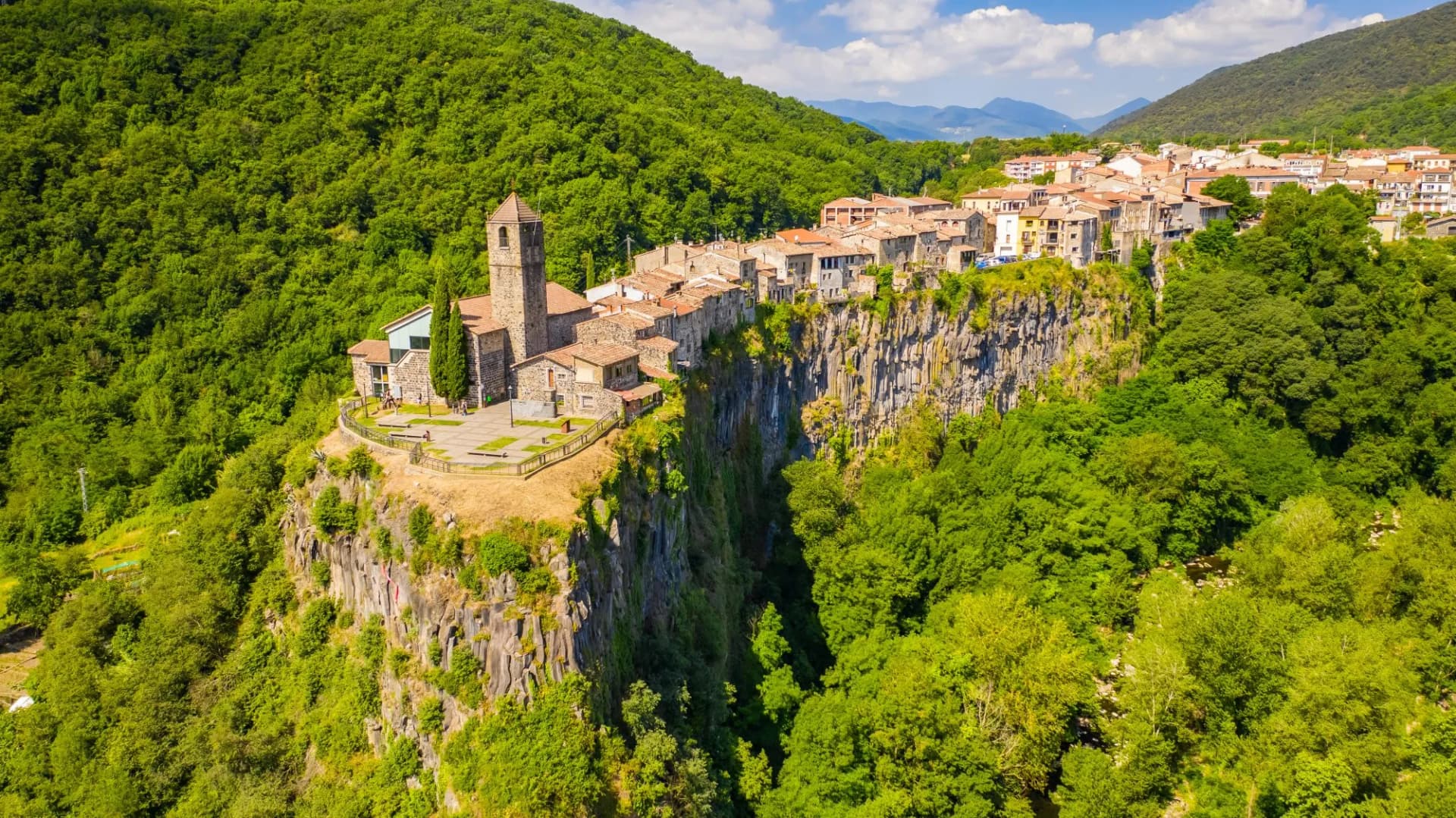 Castellfollit de la Roca village perched atop a sheer cliff surrounded by lush green mountains in Spain.